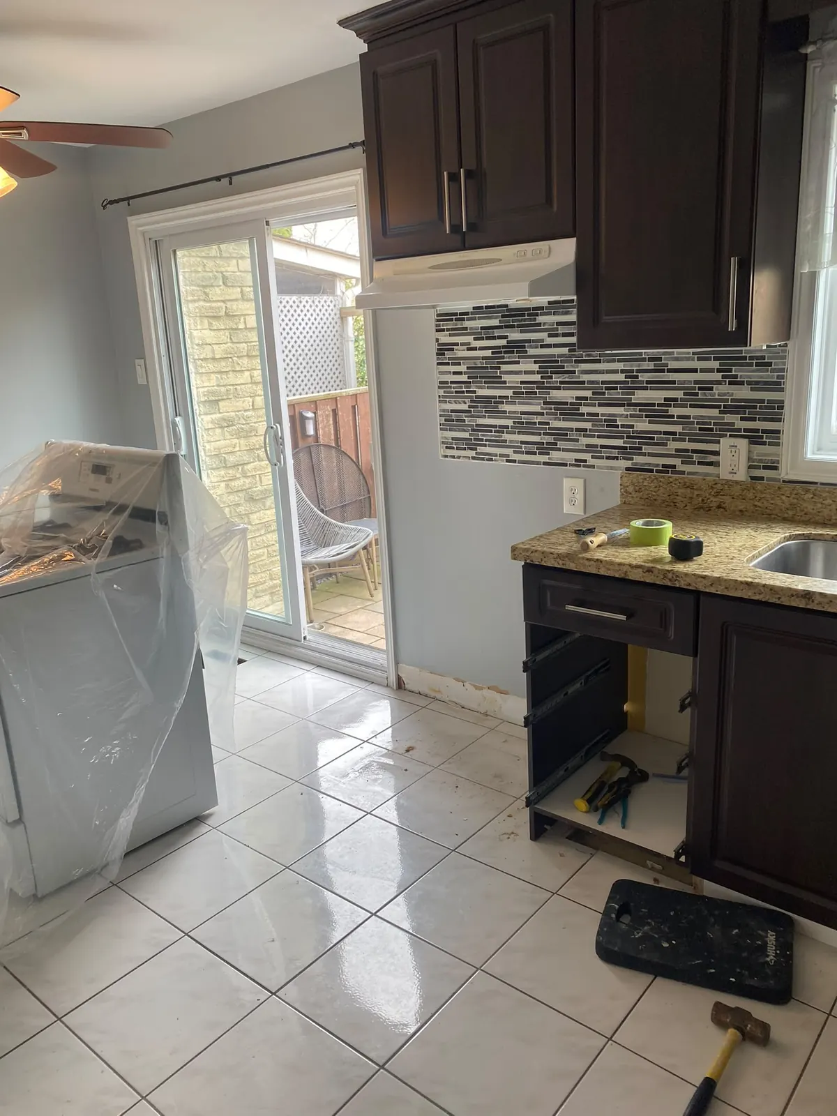 Before: dark kitchen cabinets with a glass mosaic backsplash, granite counters and white ceramic tile floor